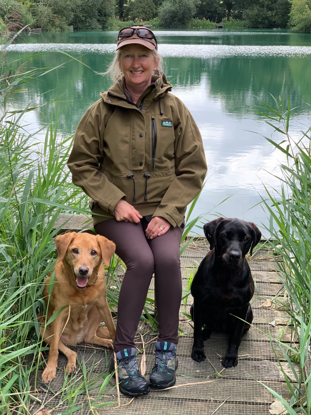 jill-thorpe-sitting-by-lake-with-two-of-her-labradors-develop-your-dog